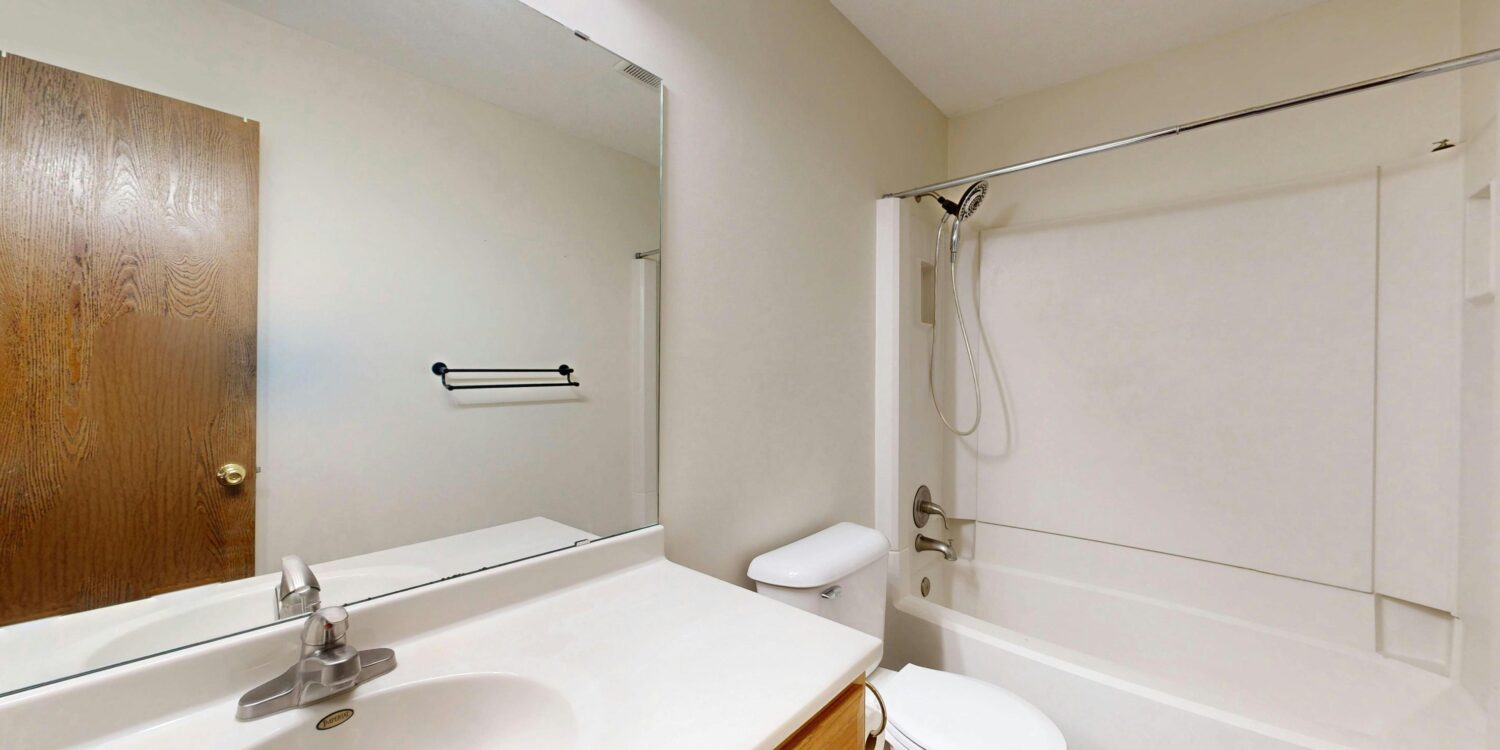 Bathroom with double-sink vanity, large mirror, toilet, and a bathtub/shower combo in a neutral-toned room.