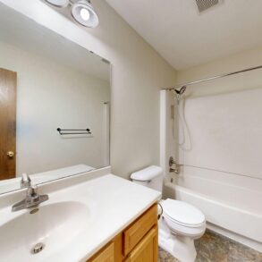 Bathroom with double-sink vanity, large mirror, toilet, and a bathtub/shower combo in a neutral-toned room.