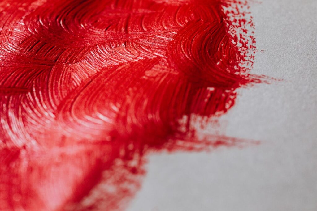 Close-up of red brushstrokes on a pale surface, forming curved patterns (abstract painting).